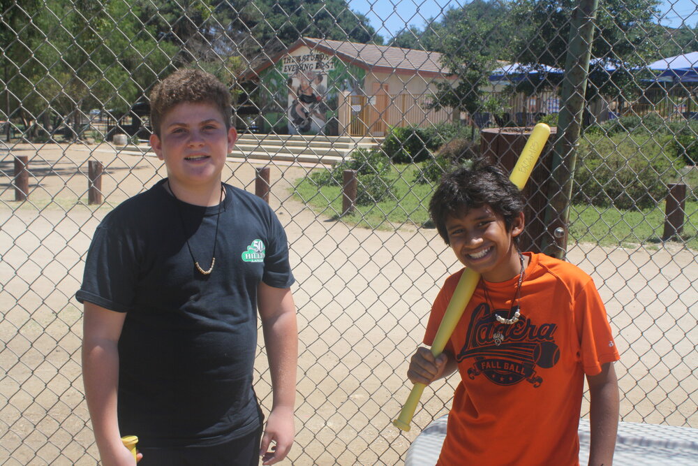Boy with baseball bat stands next to another camper